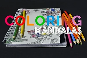 Tegneblok med halvfarvede mandala-designs og farvede blyanter på sort baggrund