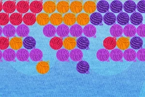 Farverige bånd af garnnøgler i røde, orange, lilla og violette nuancer mod en lyseblå baggrund