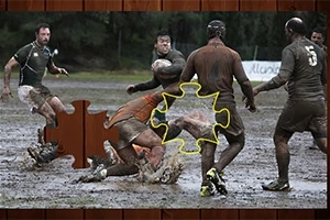 Flere mænd spiller rugby på en mudret bane med et puslespilsstykke indsat i midten