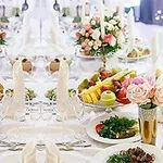 Et elegant dækket bord med blomsterdekorationer, frugtfade og tallerkener med grøntsager, omgivet af krystalglas og guldvaser