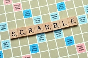 Træbrikker med bogstaverne, der staver SCRABBLE, placeret på et bræt med farvede felter