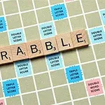 Træbrikker med bogstaverne, der staver SCRABBLE, placeret på et bræt med farvede felter