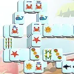 Mahjong-brikker med havtema, herunder krabber, søstjerner og hvaler, arrangeret foran en strandbaggrund